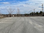 A view of an empty paved parking lot. the lot has one large crack running through the it from front to back. Some trees are seen in the background.