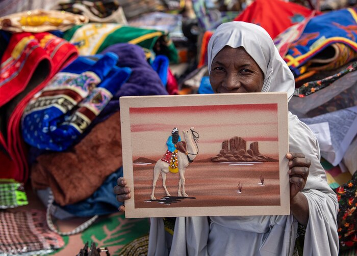 Woman holds a sandstone painting of a camel rider.