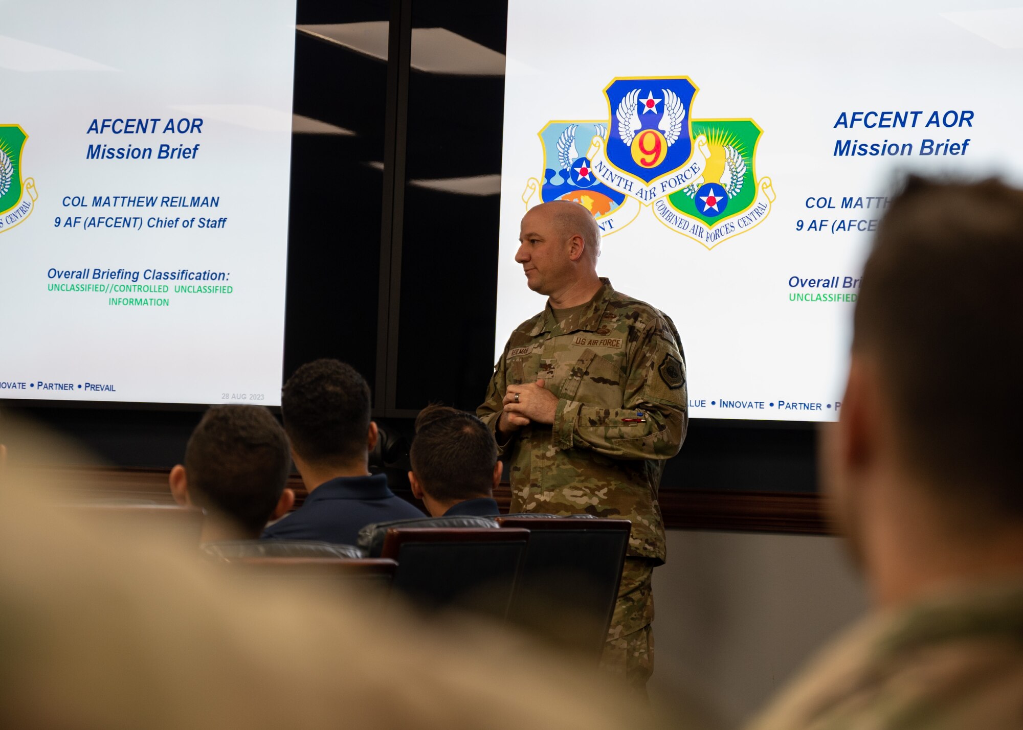 A man briefs in front of a slideshow inside a room
