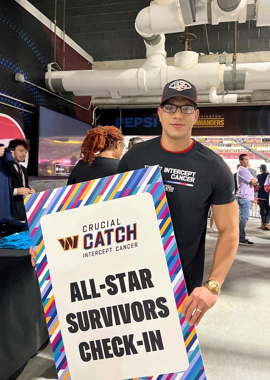 Staff Sgt. Marti holds a sign that says, "All-Star Survivors Check-In." He is shown in an area of FedEx field.