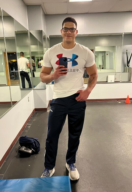 Staff Sgt. Marti takes a selfie in a mirror at a gym. He is wearing a white tshirt.