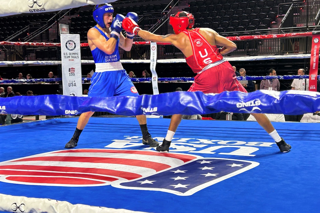 A few people in stands watch a boxer block a punch from an opponent in a blue ring with red American flag highlights.