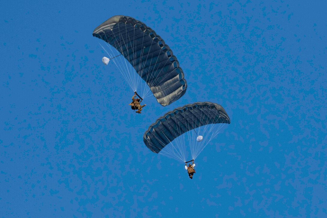 Two soldiers descend in the sky wearing parachutes.