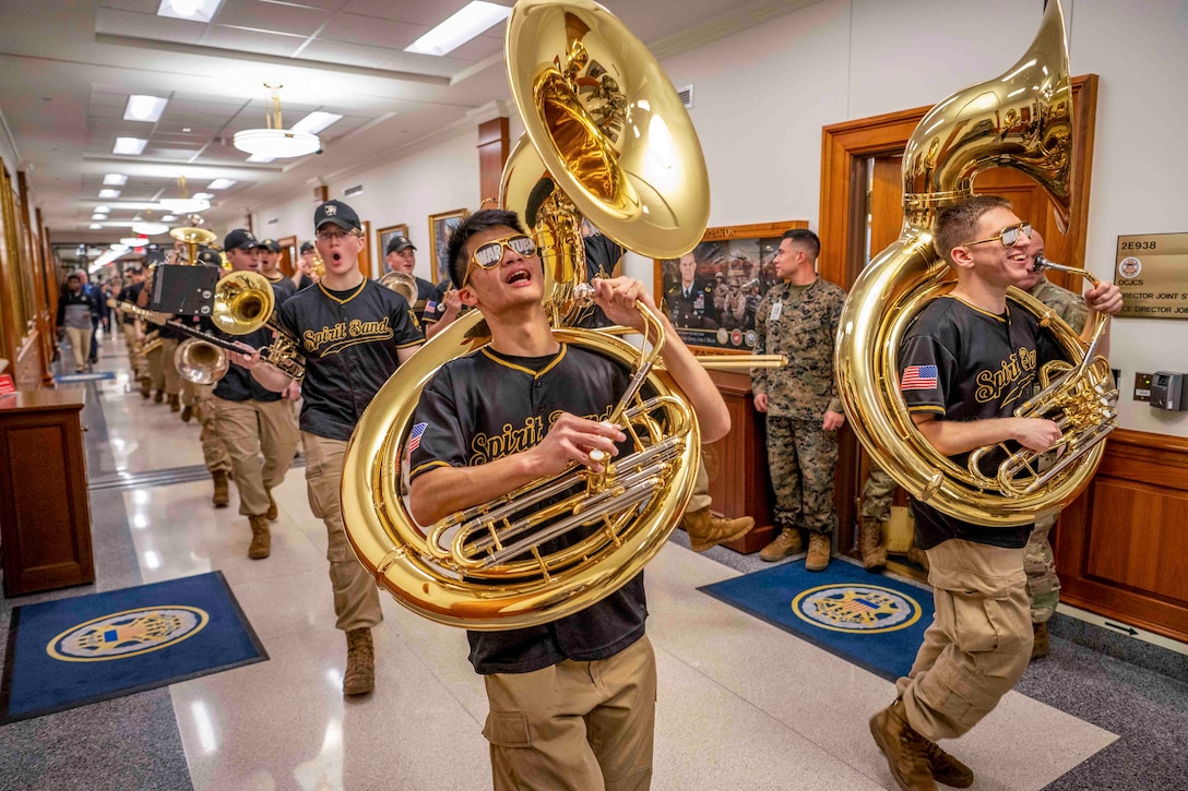 Cadets walk down a hallway while carrying instruments.