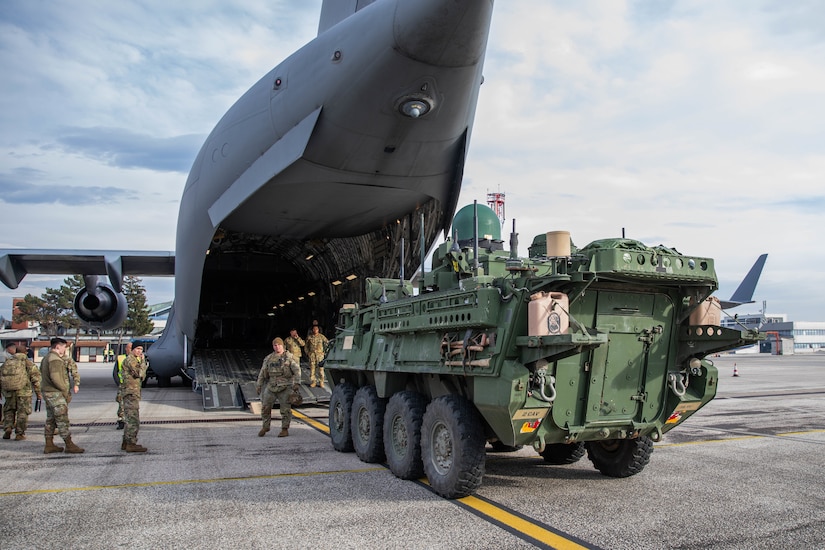 Soldiers unload armored vehicles from a parked aircraft.