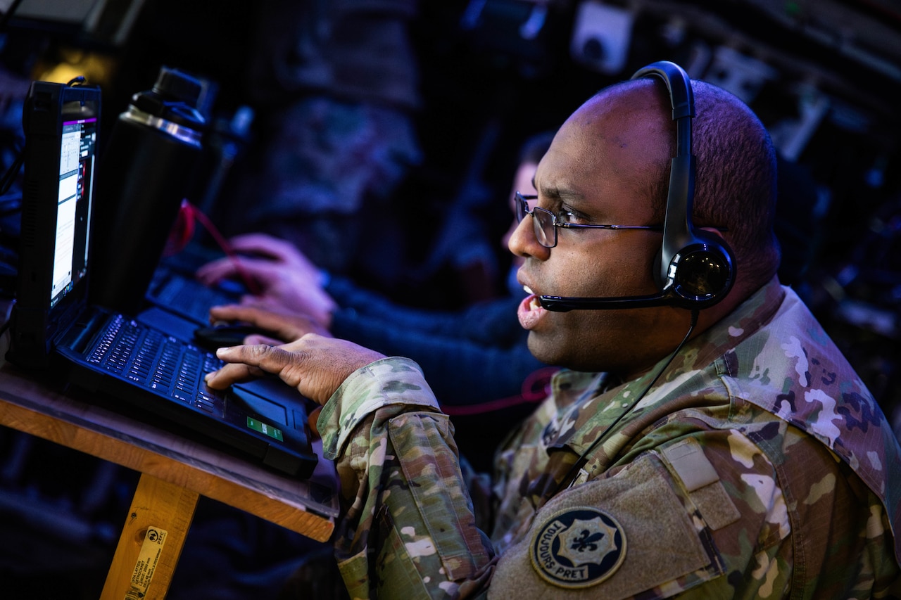 A soldier works on a laptop.
