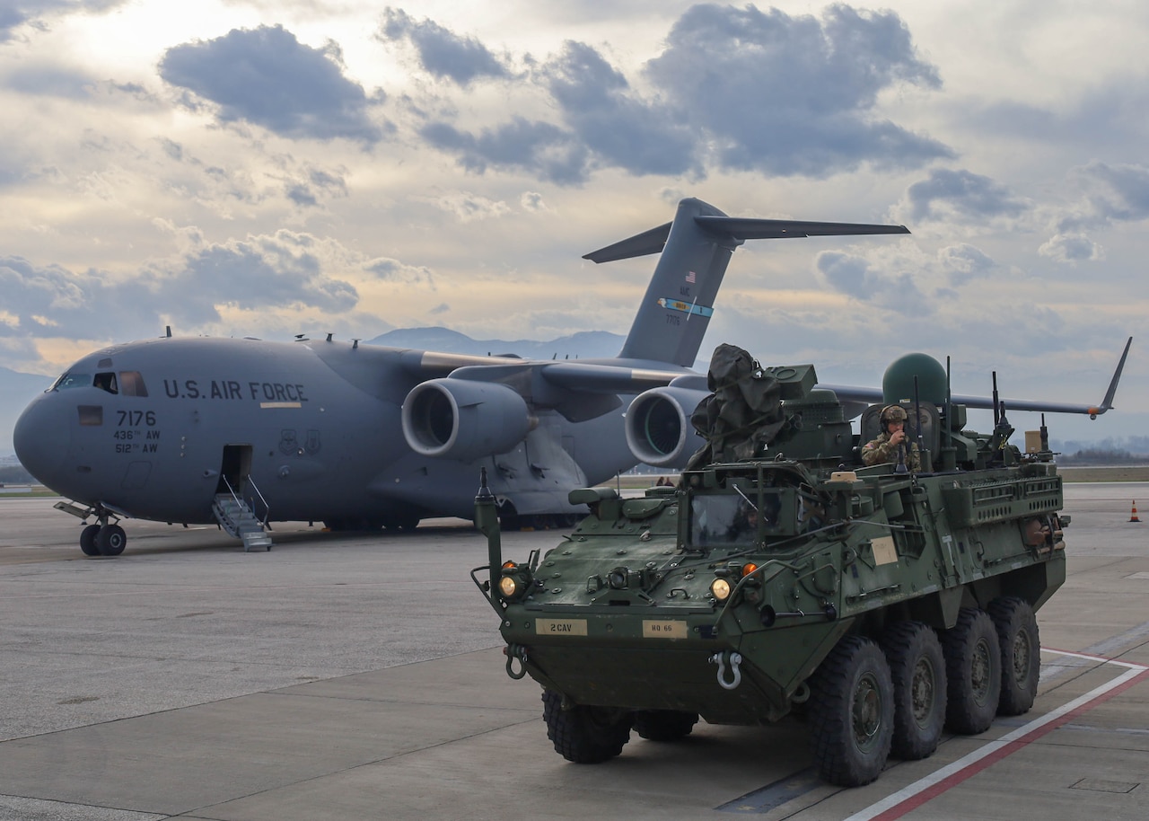 Soldiers operate a military vehicle in front of a parked aircraft.
