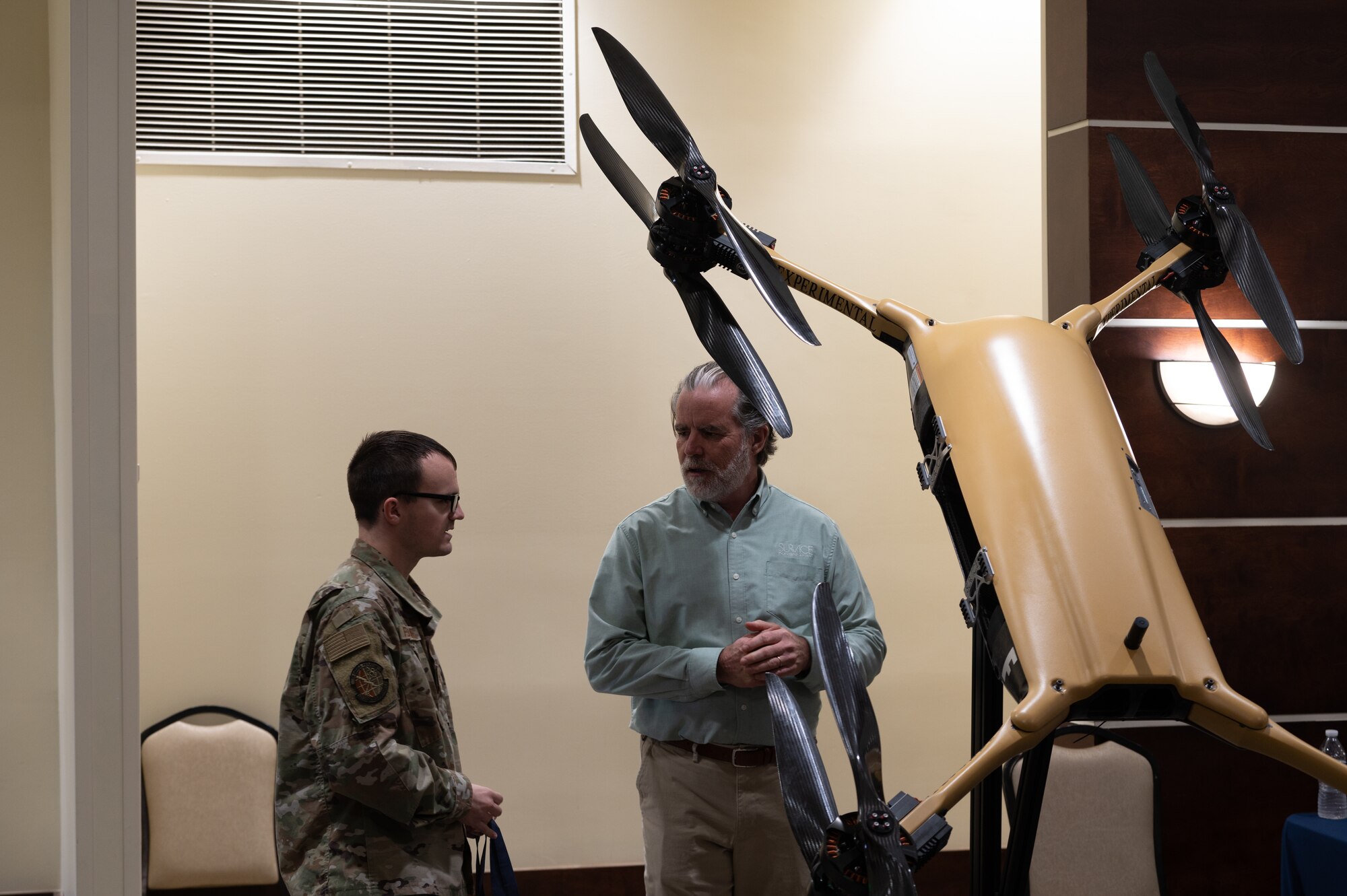 U.S. Air Force Staff Sgt. Kenneth Fernandez, noncommissioned officer in charge of traffic management assigned to 927th Logistics Readiness Squadron, and Mike Ray discuss a drone model during a technology expo at MacDill Air Force Base, Florida, Dec. 5, 2023.