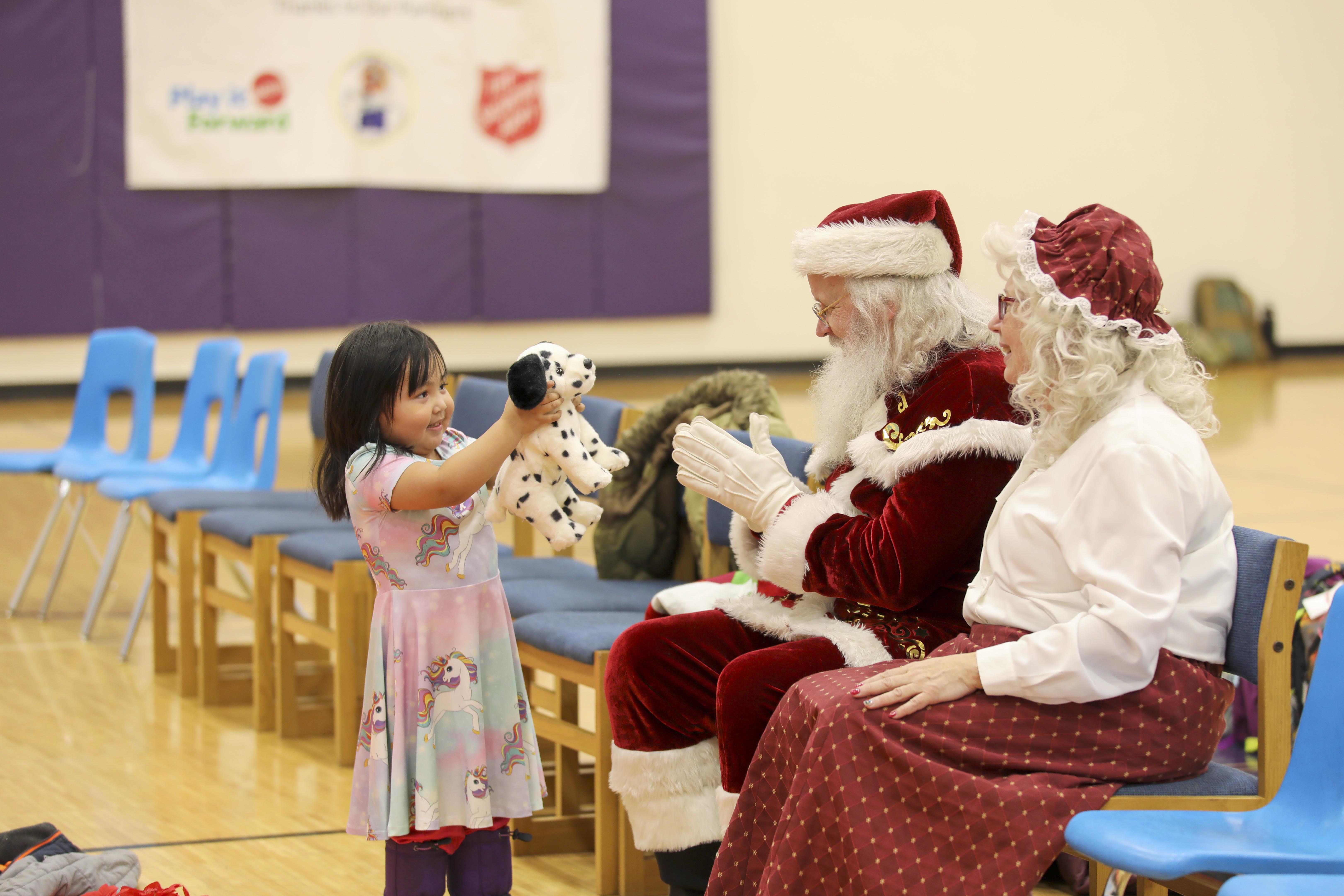 A child shows a stuffed animal to Santa and Mrs. Claus.