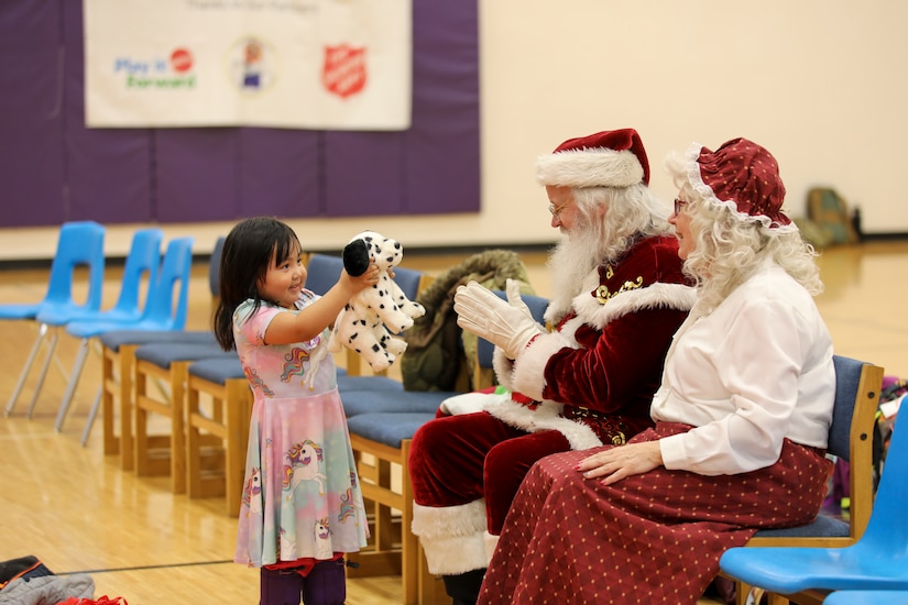 A young child shows her new toy to Santa and Mrs. Claus during Operation Santa Claus at the Martin L. Olson School gymnasium in Golovin, Alaska, Nov. 30, 2023.