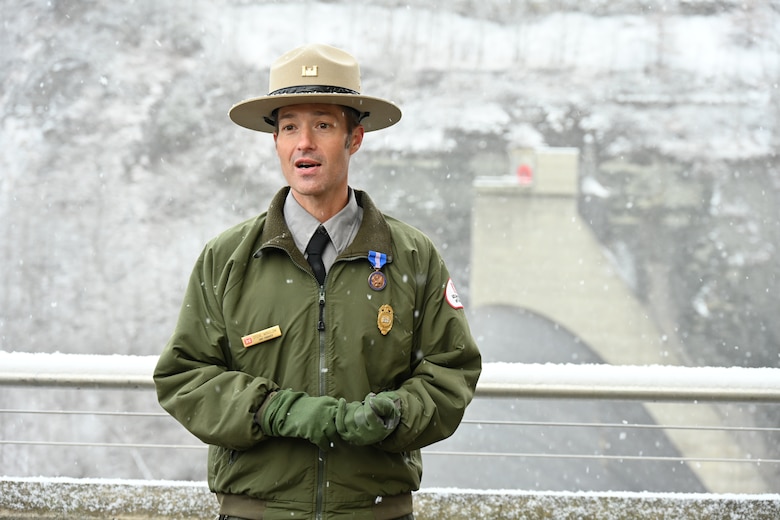 A U.S. Army Corps of Engineers Ranger stands atop a concrete dam with snow falling.