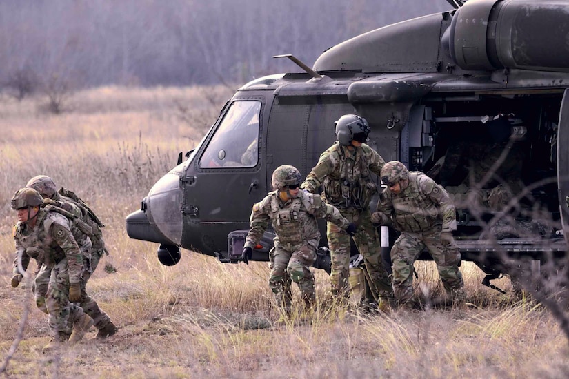 Soldiers exit a parked helicopter.