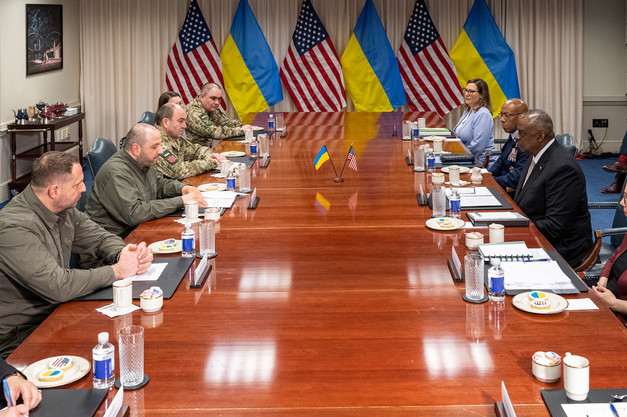 en and women in uniforms and suits sit around a conference room table.  in the rear are U.S. and Ukrainian flags.