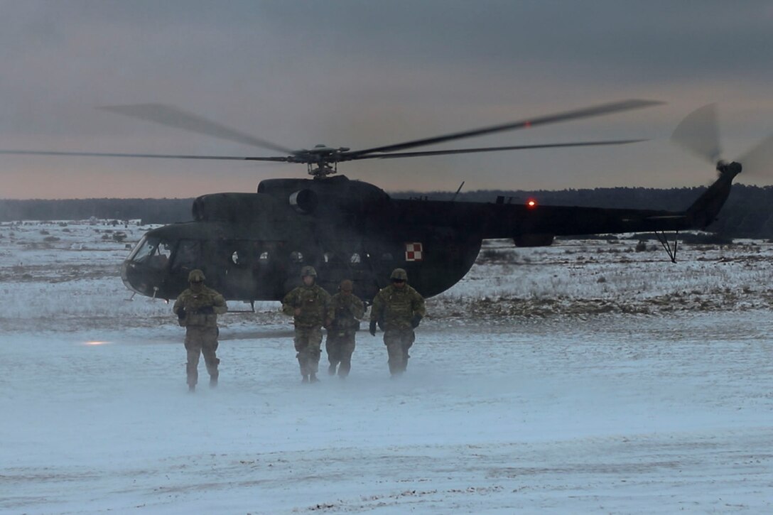 Soldiers exit a helicopter on a snowy field.