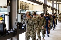 Servicemembers in U.S. military uniforms firing pistols on indoor pistol range.