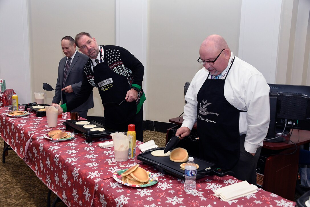 Three men cooking pancakes on a griddle