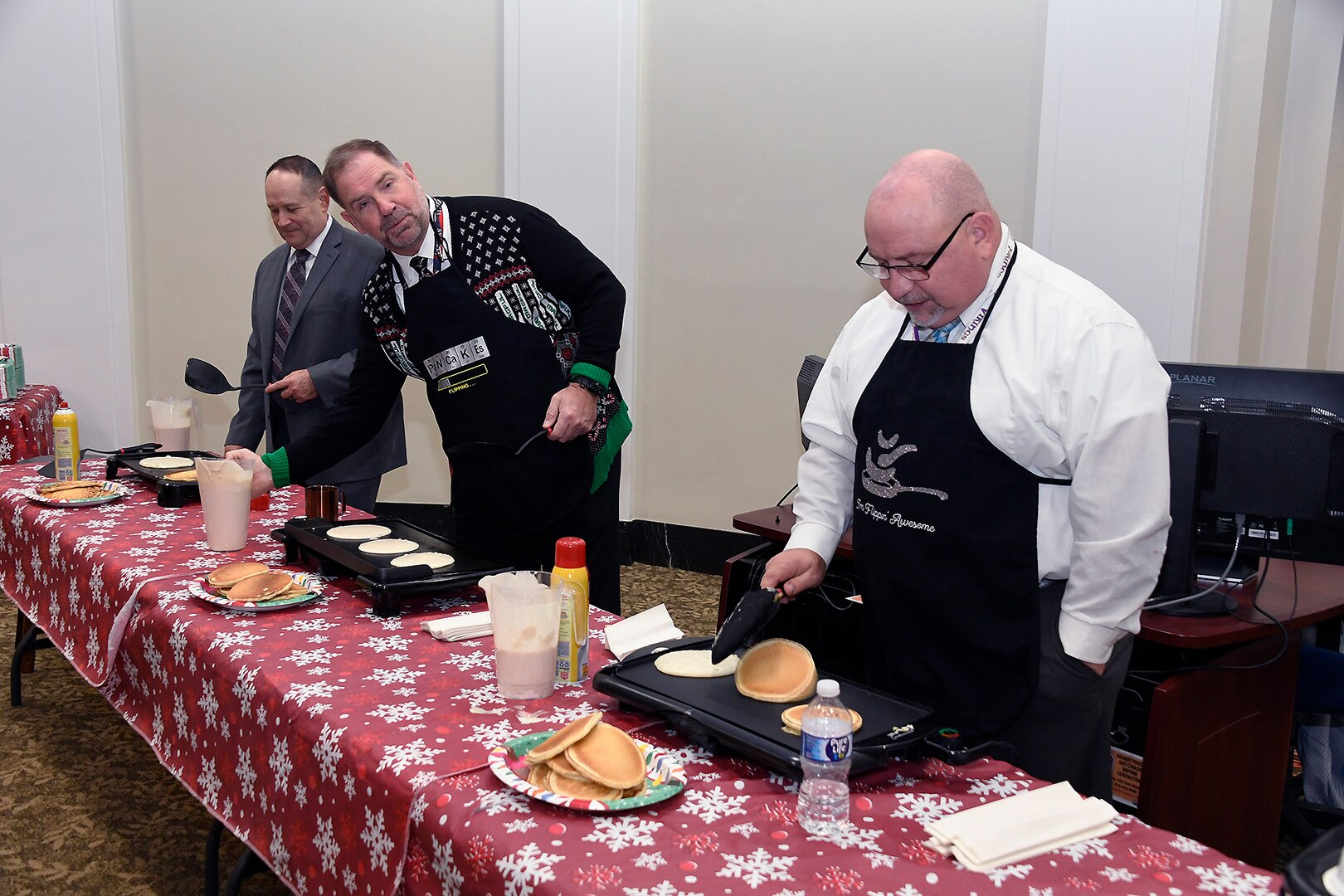 Three men cooking pancakes on a griddle