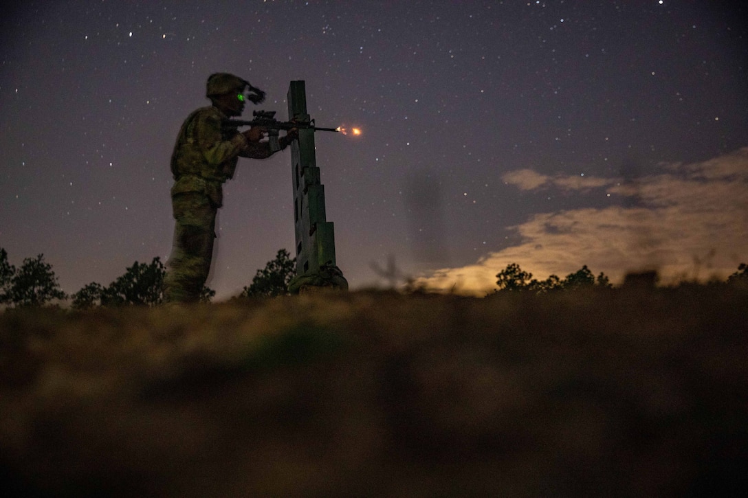 A soldier fires a rifle at night. A starry sky can be seen in the background.