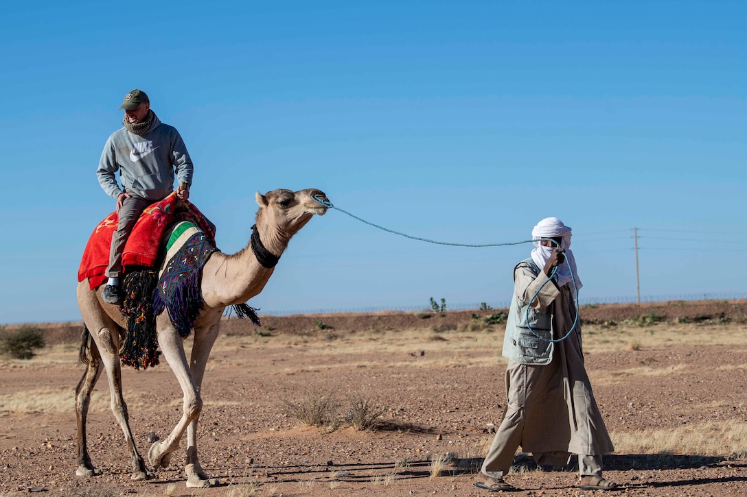 An airman rides a camel as a person leads the camel with a rope.