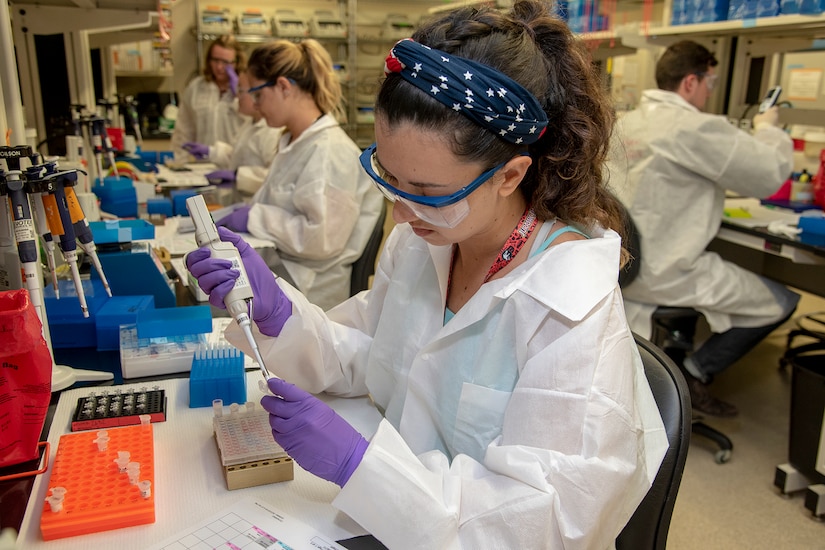 A scientist uses a tool to put a sample into a small vial in a lab.