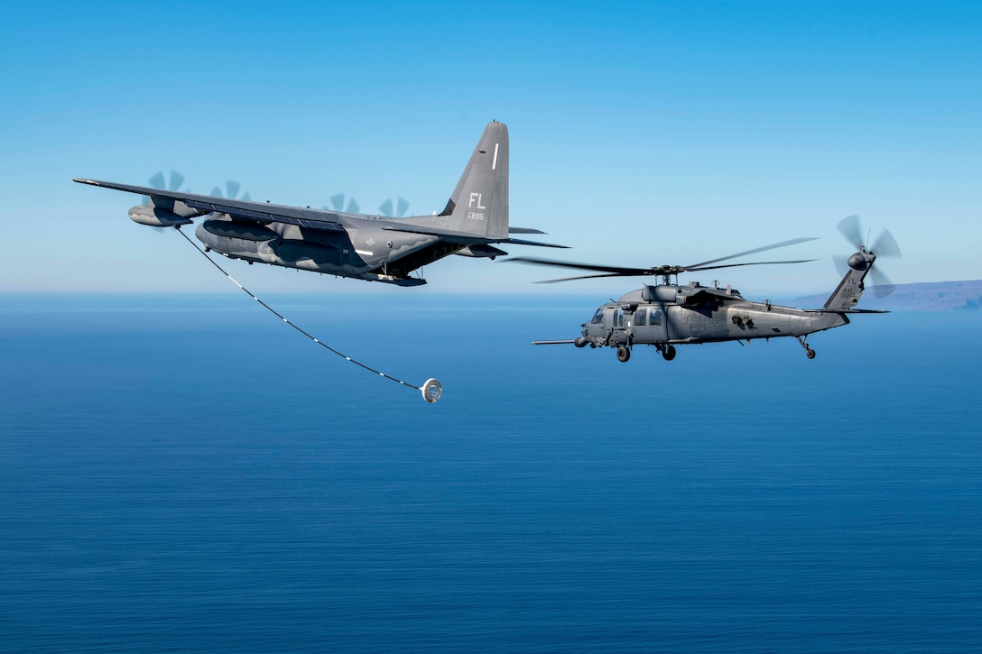 An aircraft extends its boom to a helicopter while flying over a body of water.