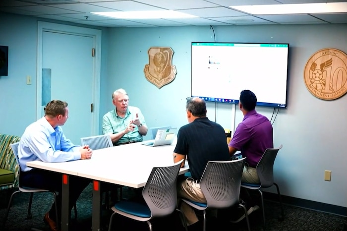 Foman and three teammates talking in a conference room
