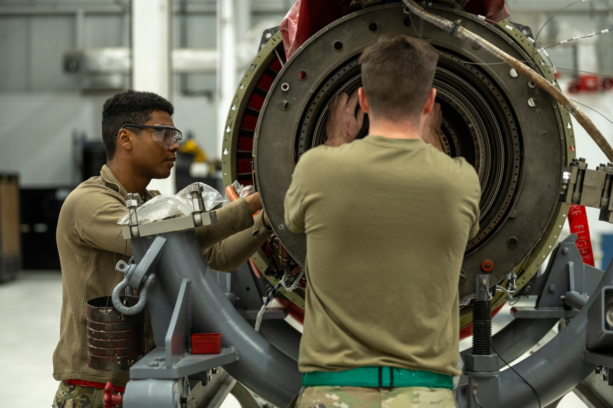 A photo of two Airmen working along-side each other, working on an aircraft engine.