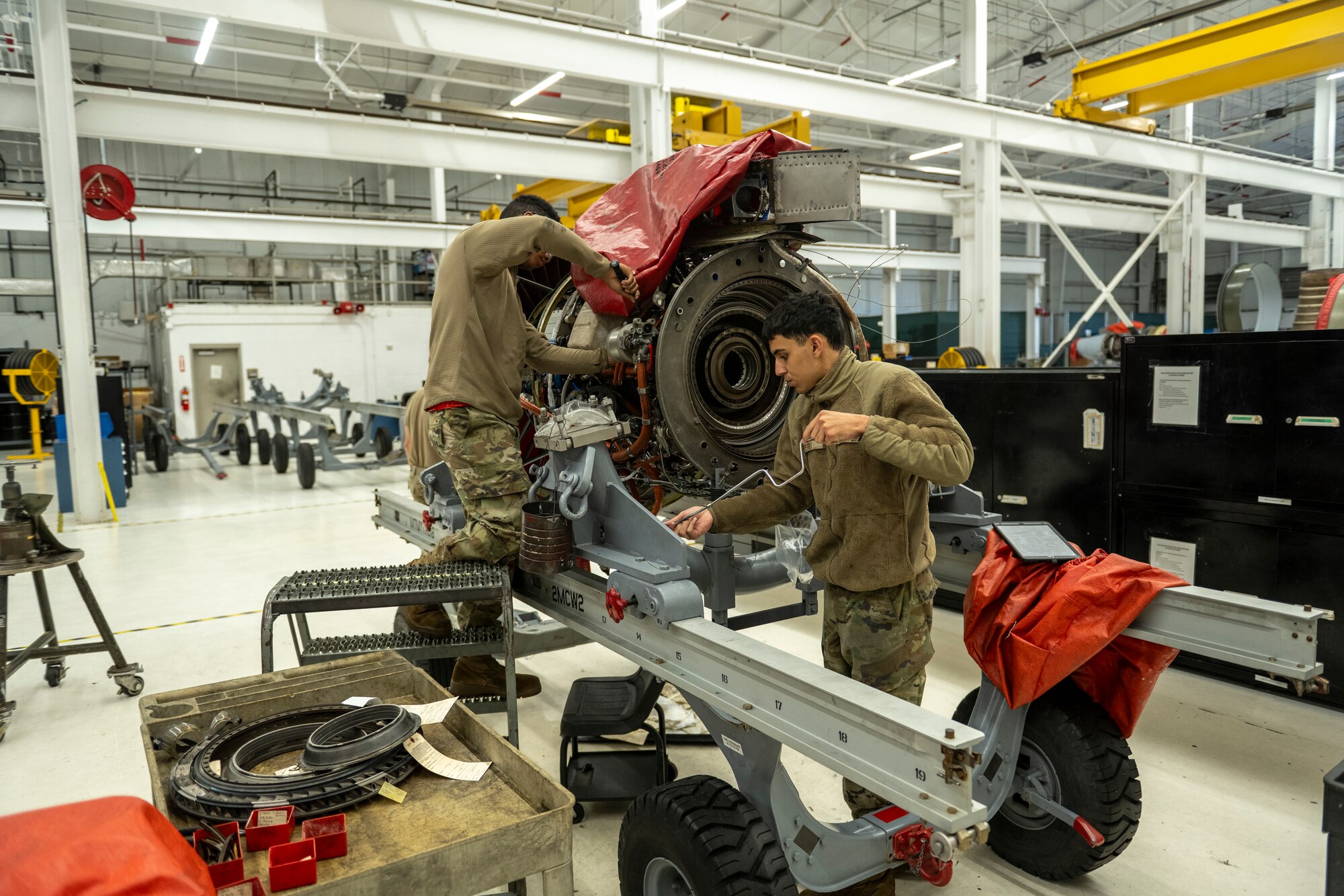 A photo of two people working along-side each other, working on an aircraft engine.