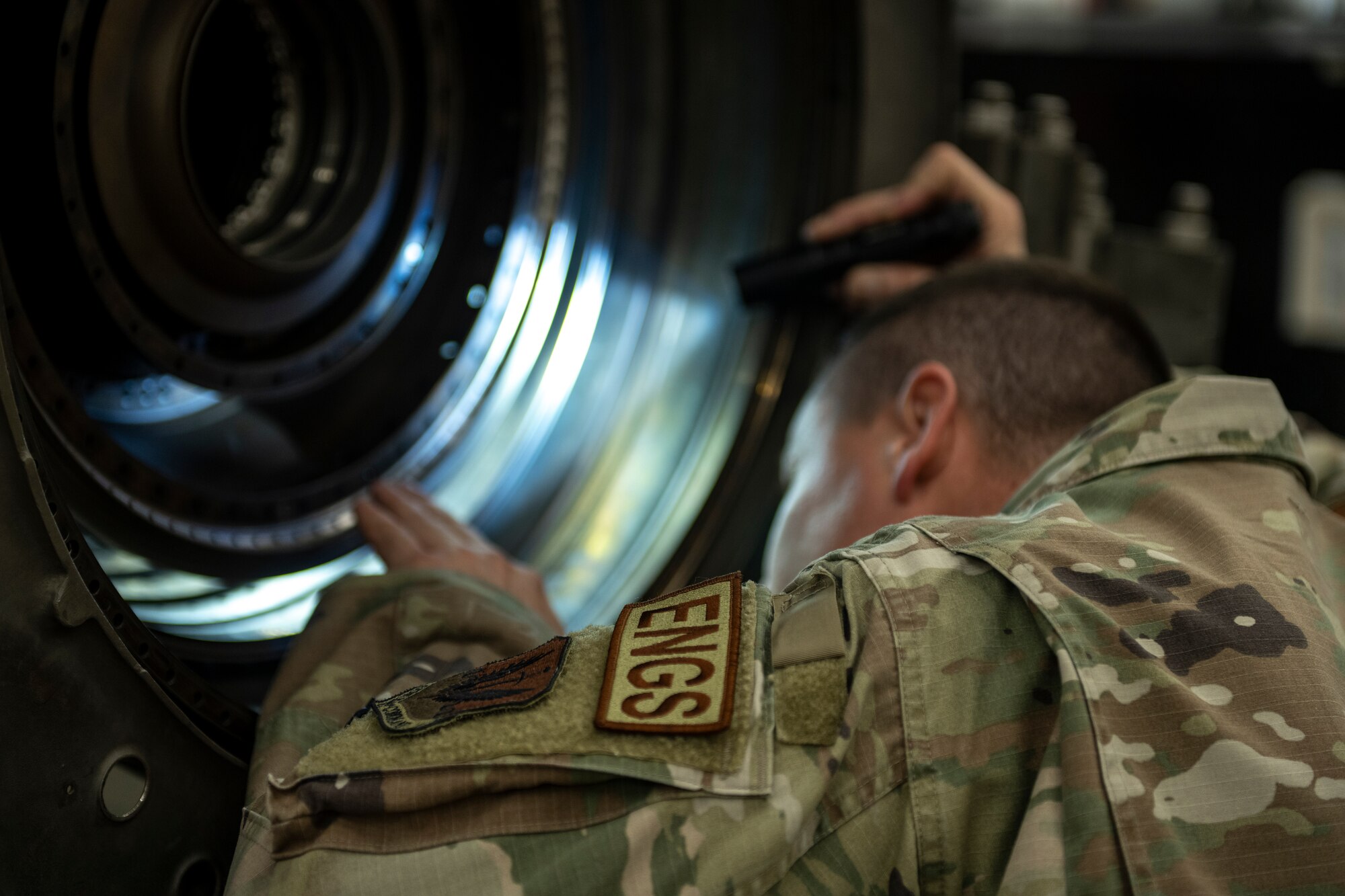 A photo of a person holding a flashlight up to an aircraft engine.