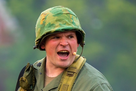 An Army Soldier wearing a camouflage helmet is yelling or singing.