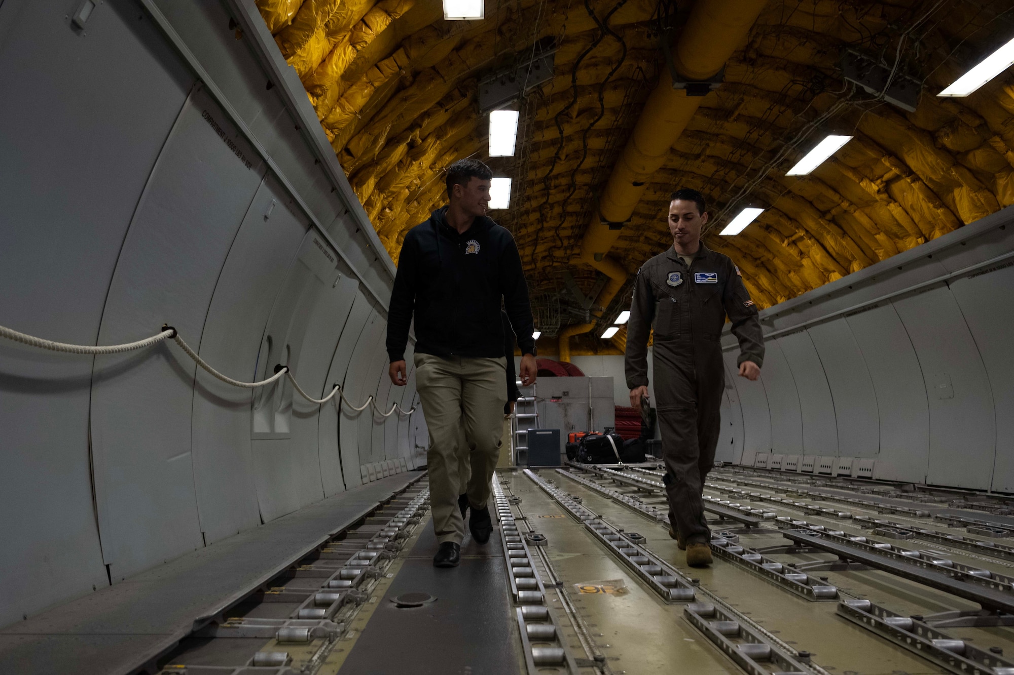 An Airman walks with a cadet through the cargo hold of a military aircraft