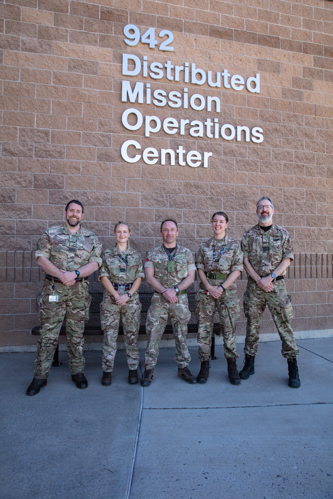 uniformed military members stand in front of brick building with lettering “942 Distributed Mission Operations Center”