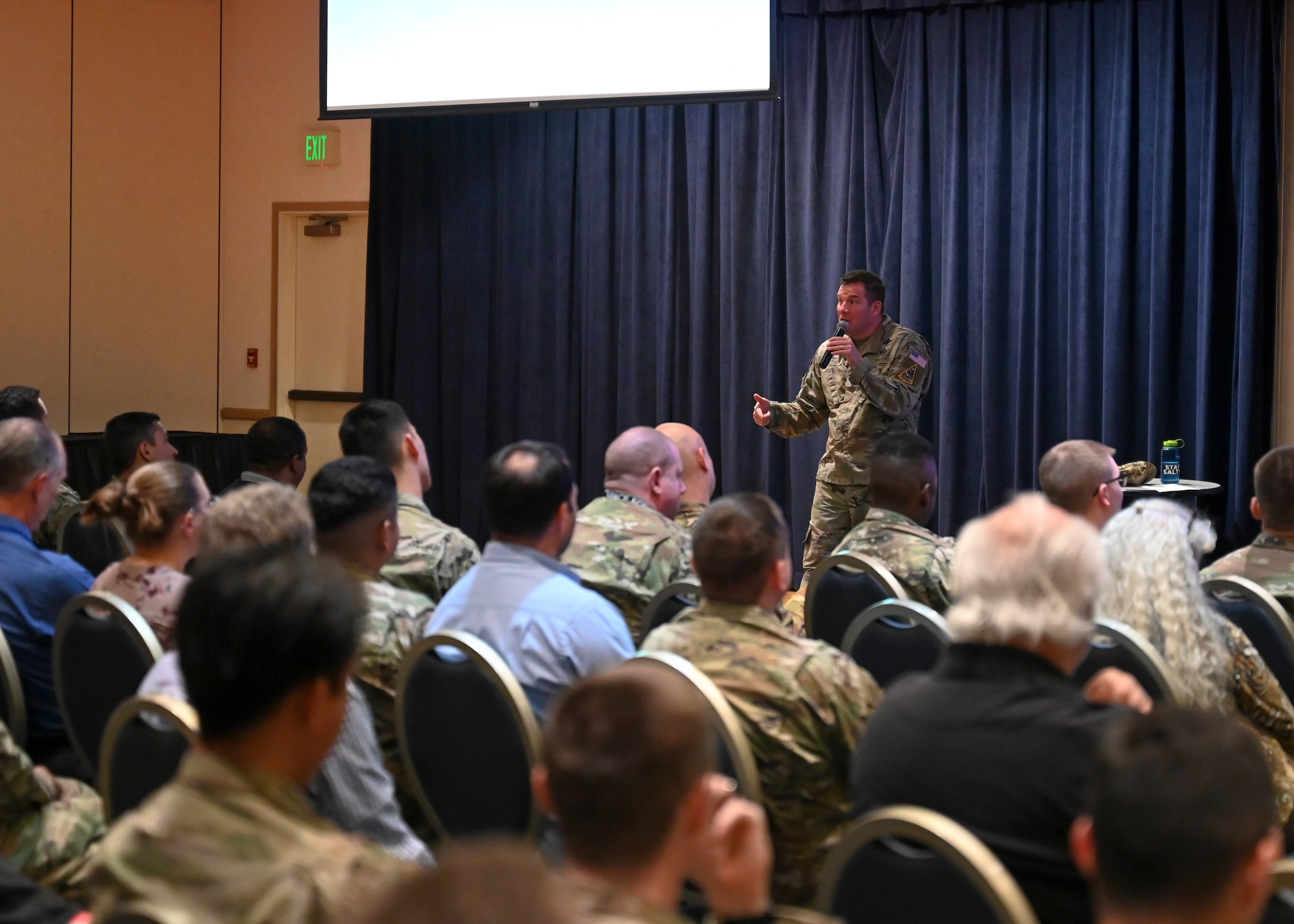 Colonel Titus speaks to a seated crowed.