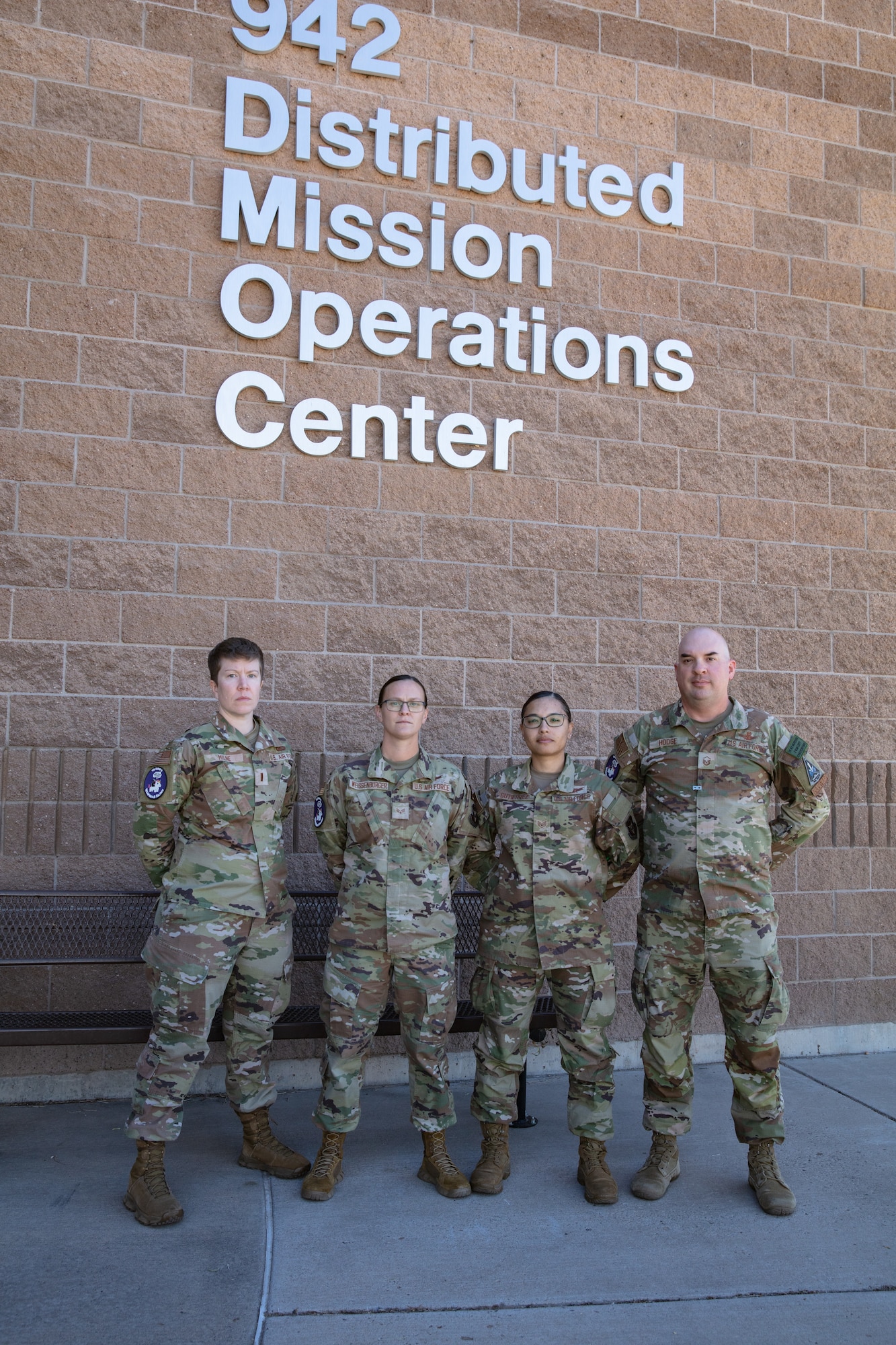 Alt text: uniformed military members stand in front of brick building with lettering “942 Distributed Mission Operations Center”