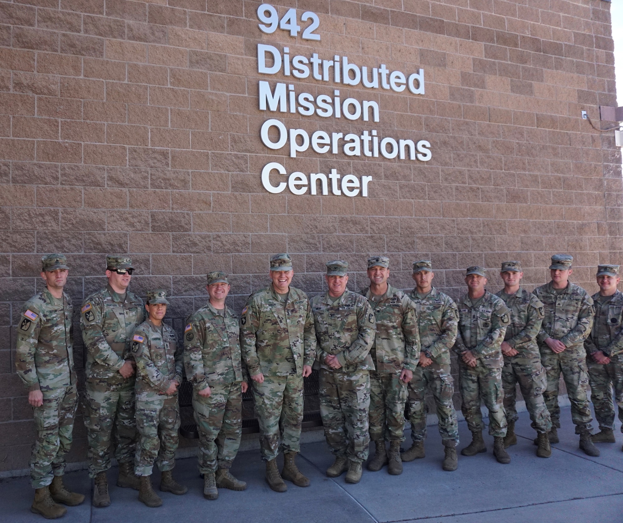 Alt text: uniformed military members stand in front of brick building with lettering “942 Distributed Mission Operations Center”