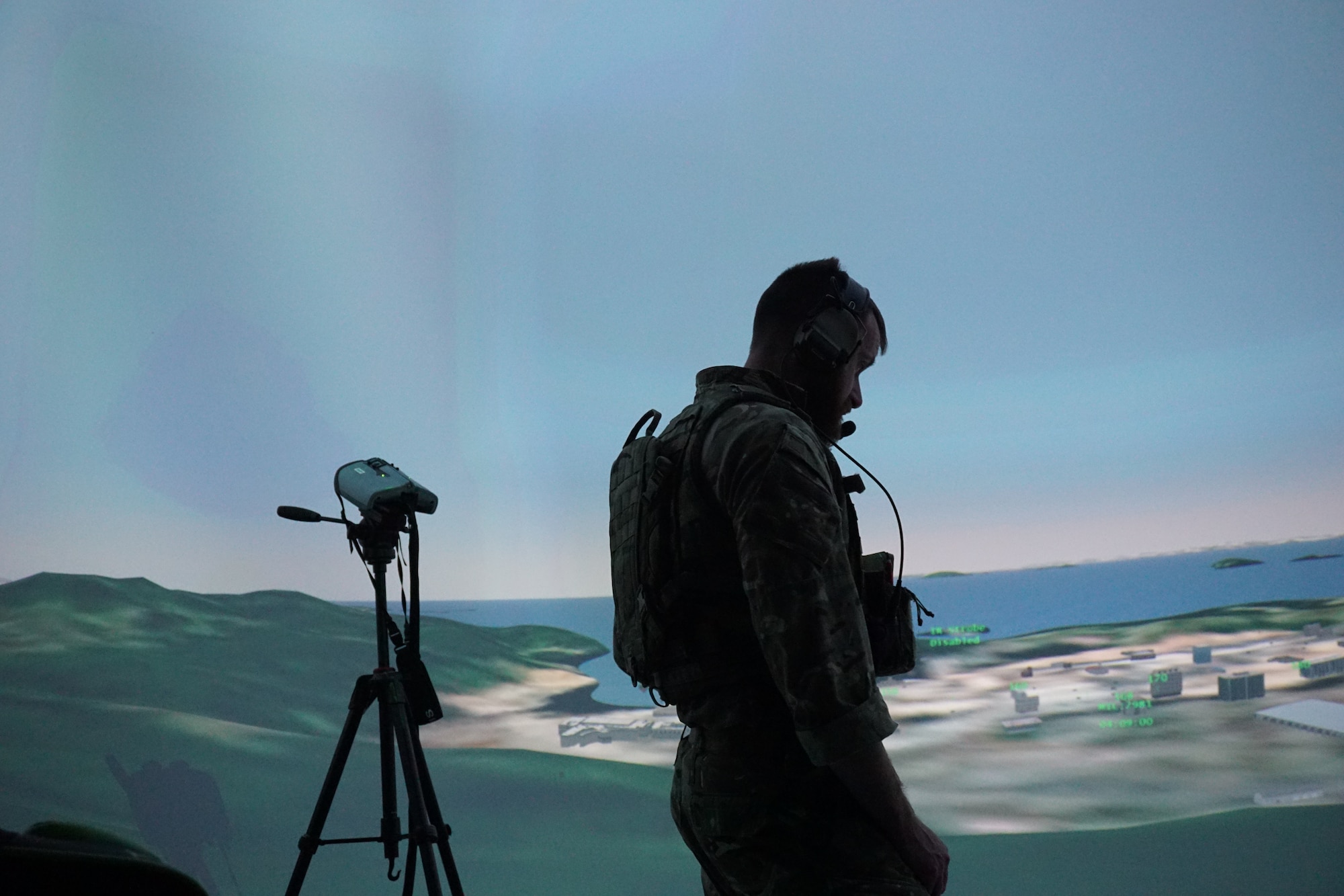 a uniformed Royal Air Force member stands next to binoculars that are mounted on a tripod while working in a virtual simulated environment