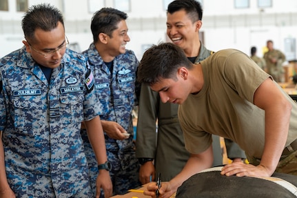 Photo of Royal Malaysian Air Force and U.S. Air Force personnel rigging an Operation Christmas Drop bundle for air drop