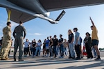 A group of young people stand a group and listen to two people in uniform.