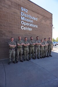 Alt text: uniformed military members stand in front of brick building with lettering “942 Distributed Mission Operations Center”