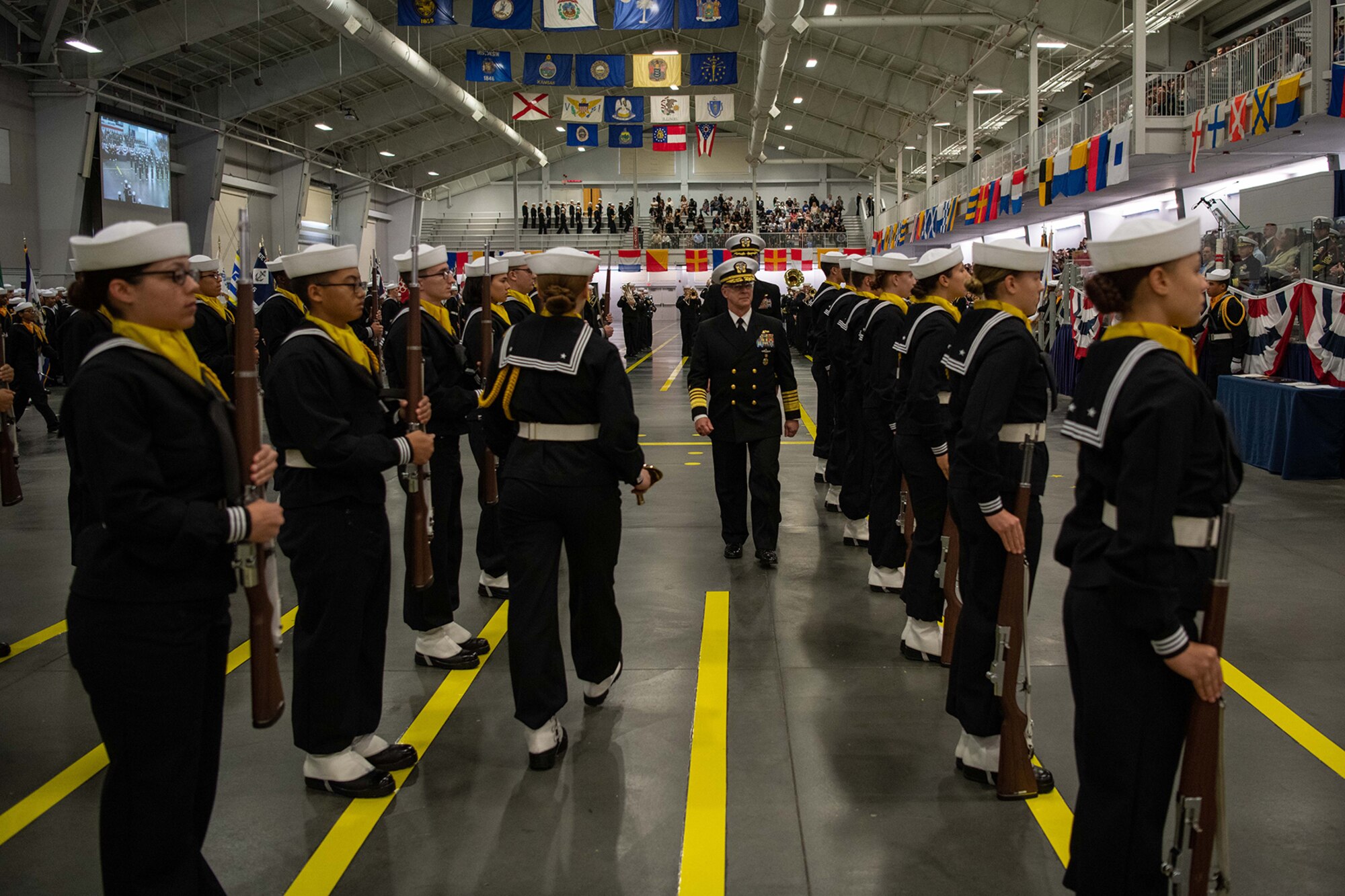Two people in officers uniforms walk between rows of a Navy honor guard.