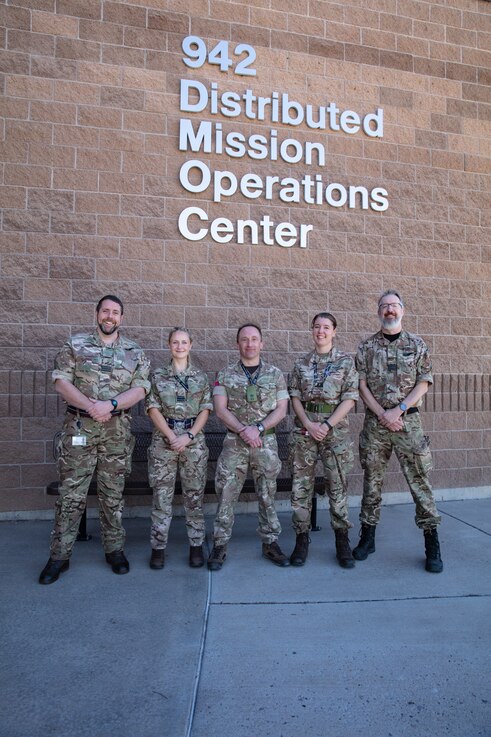  uniformed military members stand in front of brick building with lettering “942 Distributed Mission Operations Center”