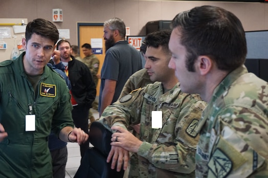  uniformed military members talking near flight simulators