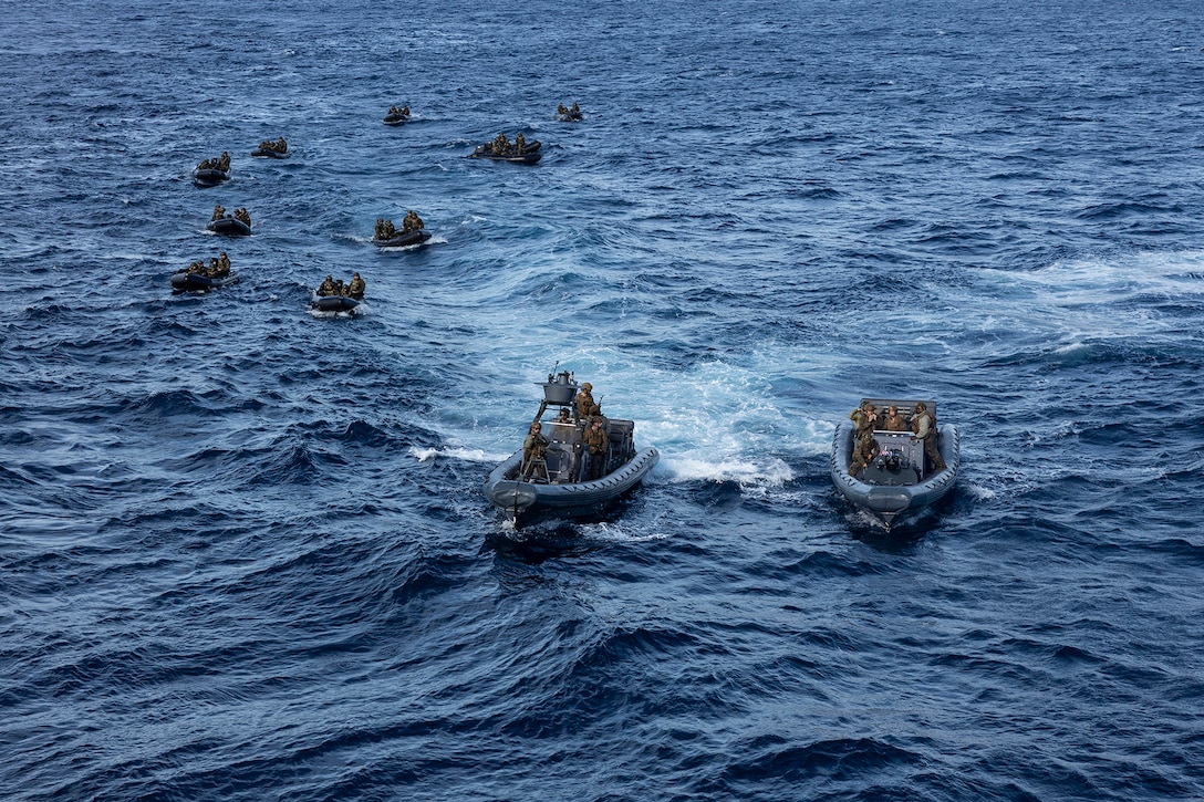 Service members sail in small boats in open water during daylight.