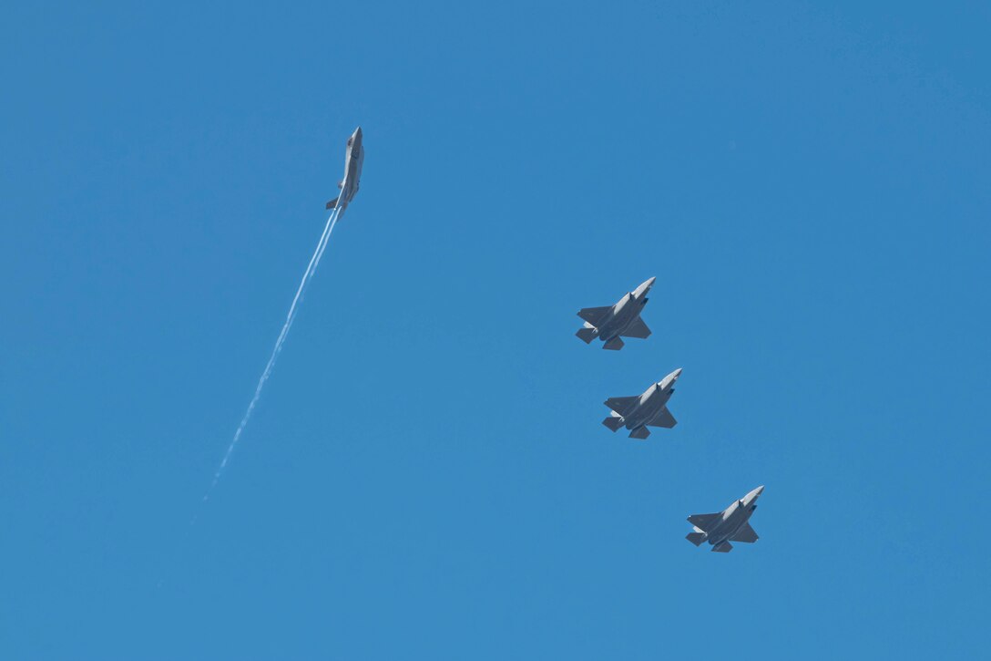 Three aircraft fly in formation to the right as another aircraft flies at an angle to the left.