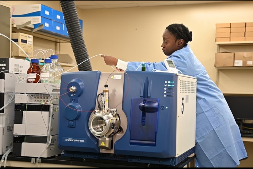 A woman holds a straw-like tube over top a large machine.