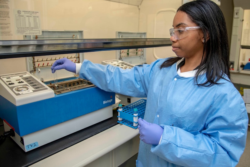 A woman in a lab coat puts a vial in a machine.