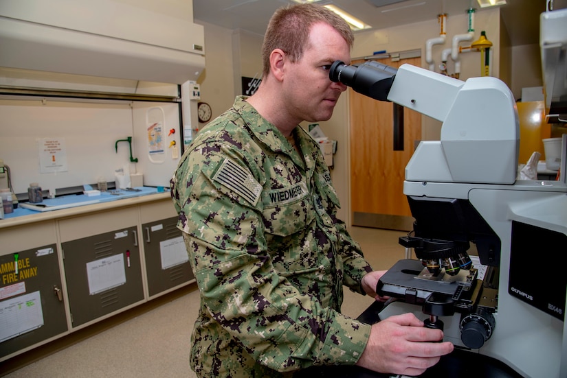 A man looks into a microscope while adjusting a nodule.