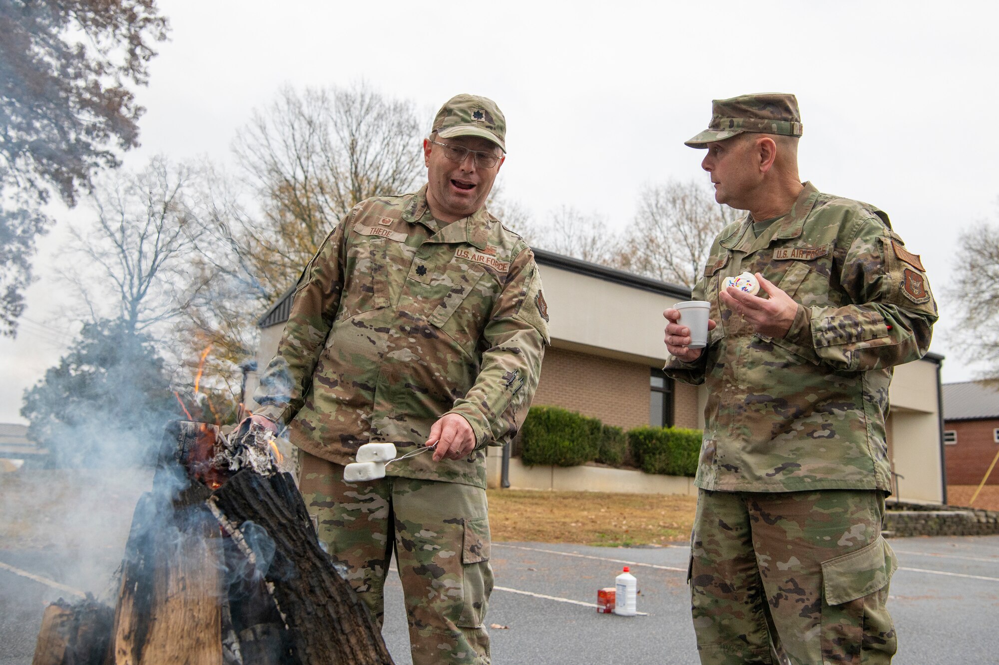 two people in military uniforms stand outside and roast marshmallows over a fire