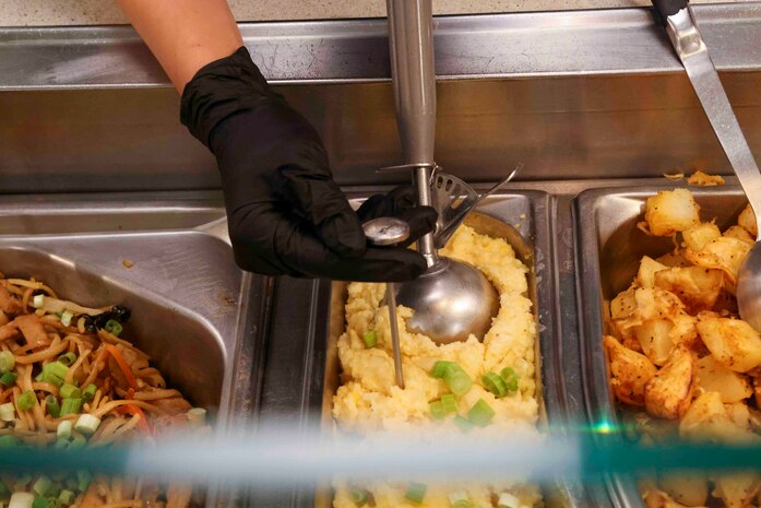 U.S. Air Force Airman 1st Class Trieu Do, 9th Force Support Squadron food service specialist, checks the temperature of food on the line at the Contrails Dining Facility on Beale Air Force Base, California, Nov. 17, 2023.
