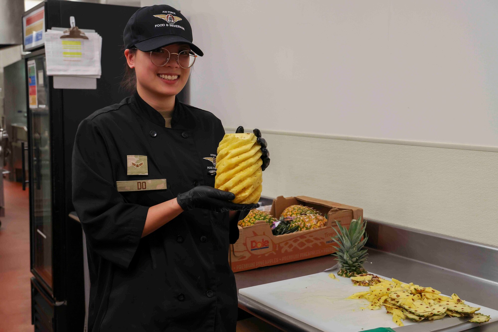 U.S. Air Force Airman 1st Class Trieu Do, 9th Force Support Squadron food service specialist, poses with a pineapple she deseeded at the Contrails Dining Facility on Beale Air Force Base, California, Nov. 17, 2023.